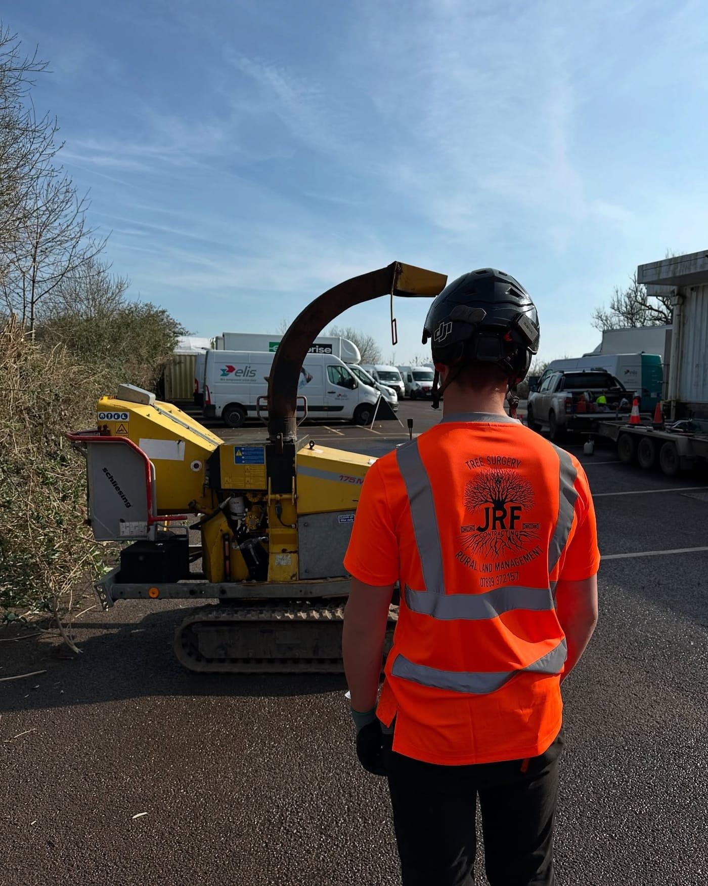 A JRF Contracting operator in branded high-visibility clothing beside a wood chipper at a roadside worksite
