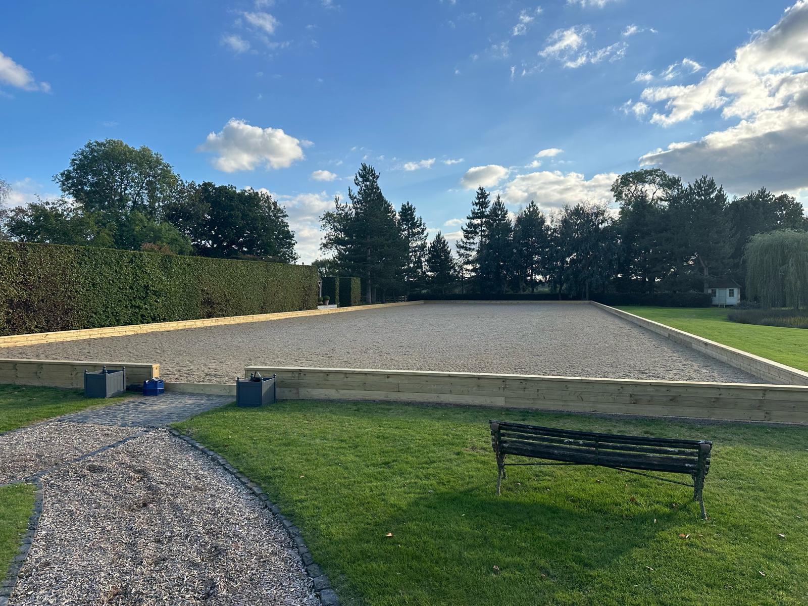 A completed equine arena with a fresh sand surface and new timber edging boards, clipped hedge behind