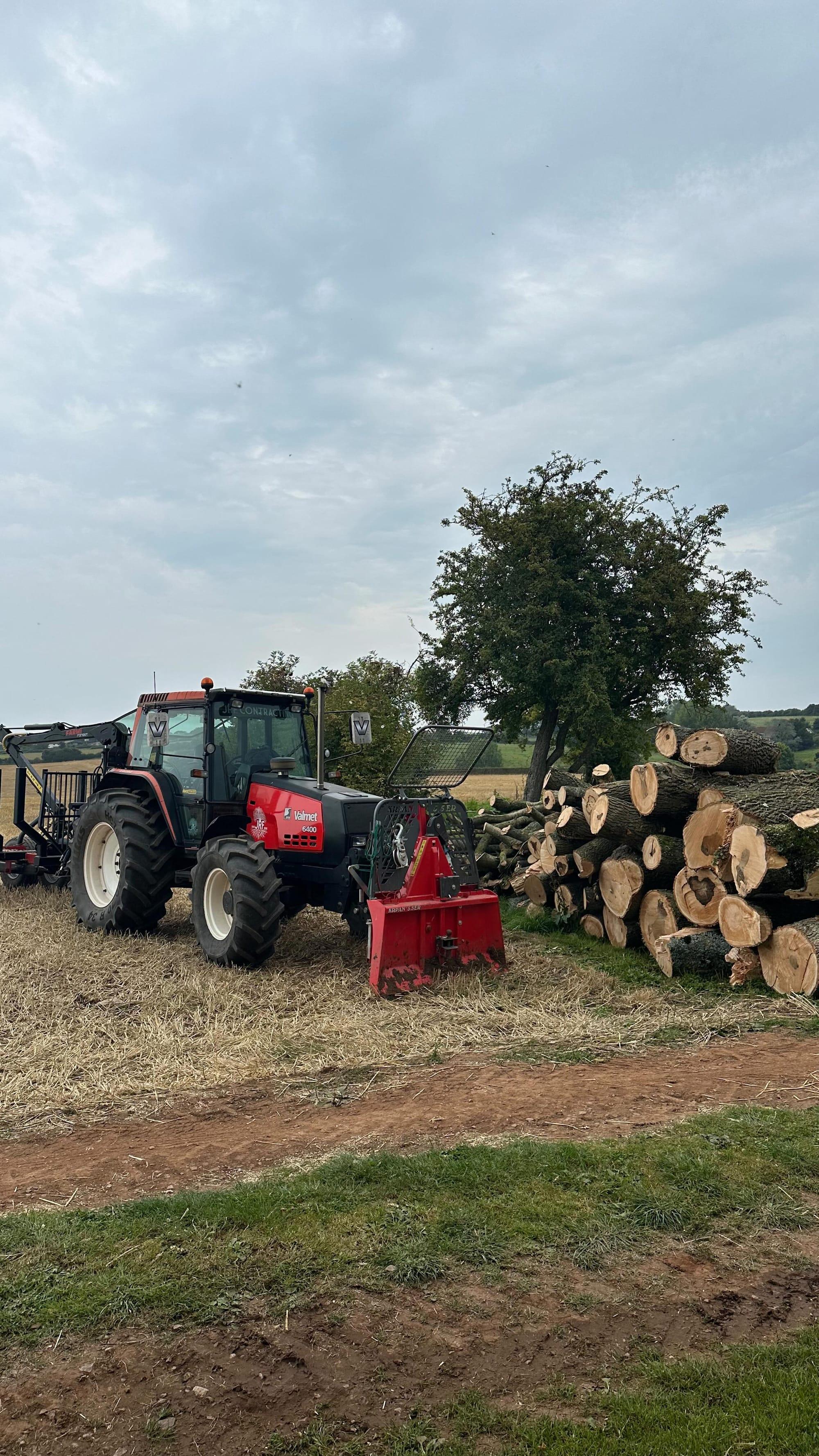 Tractor beside cut timber stacked at the edge of woodland