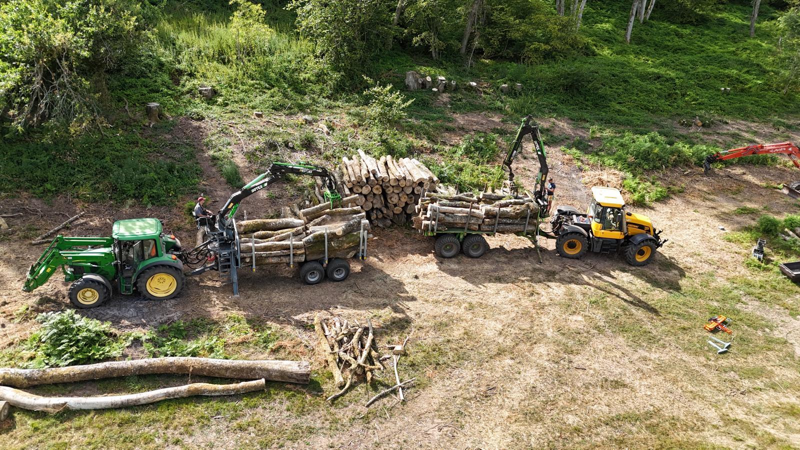 Aerial view of a tractor and a loading shovel filling timber trailers at the edge of woodland