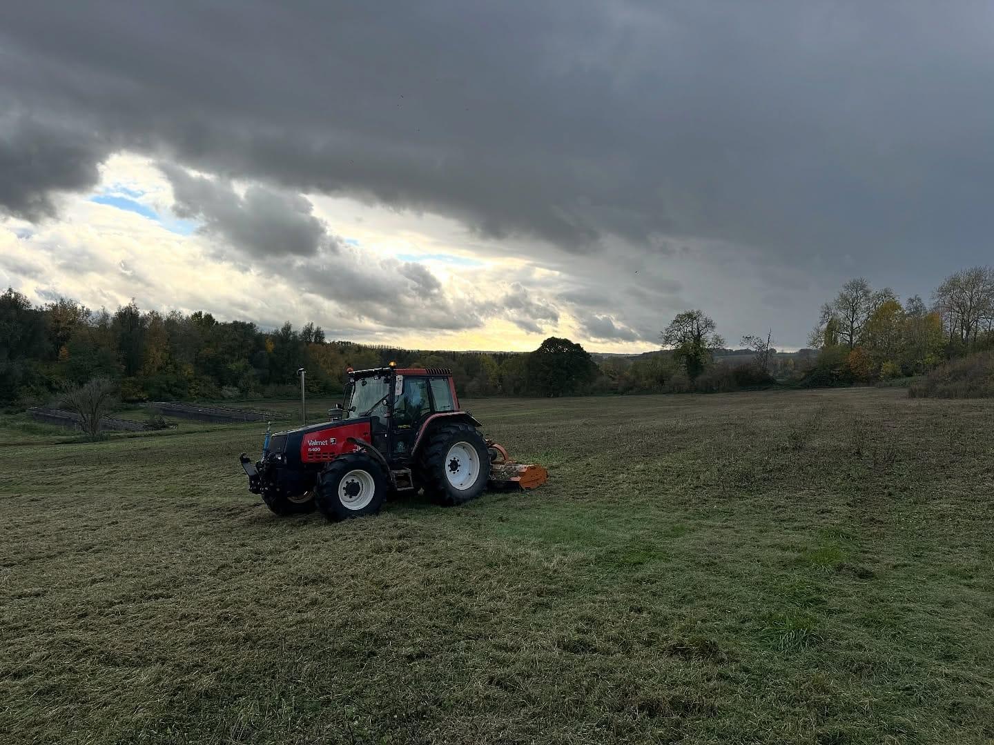 Tractor and flail mower working along a field boundary at dusk