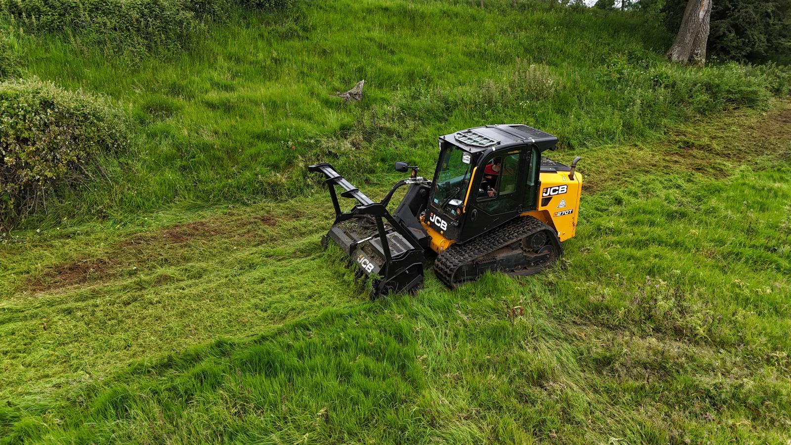 A tracked mulcher cutting a swathe through heavy rough grass on a clearance job