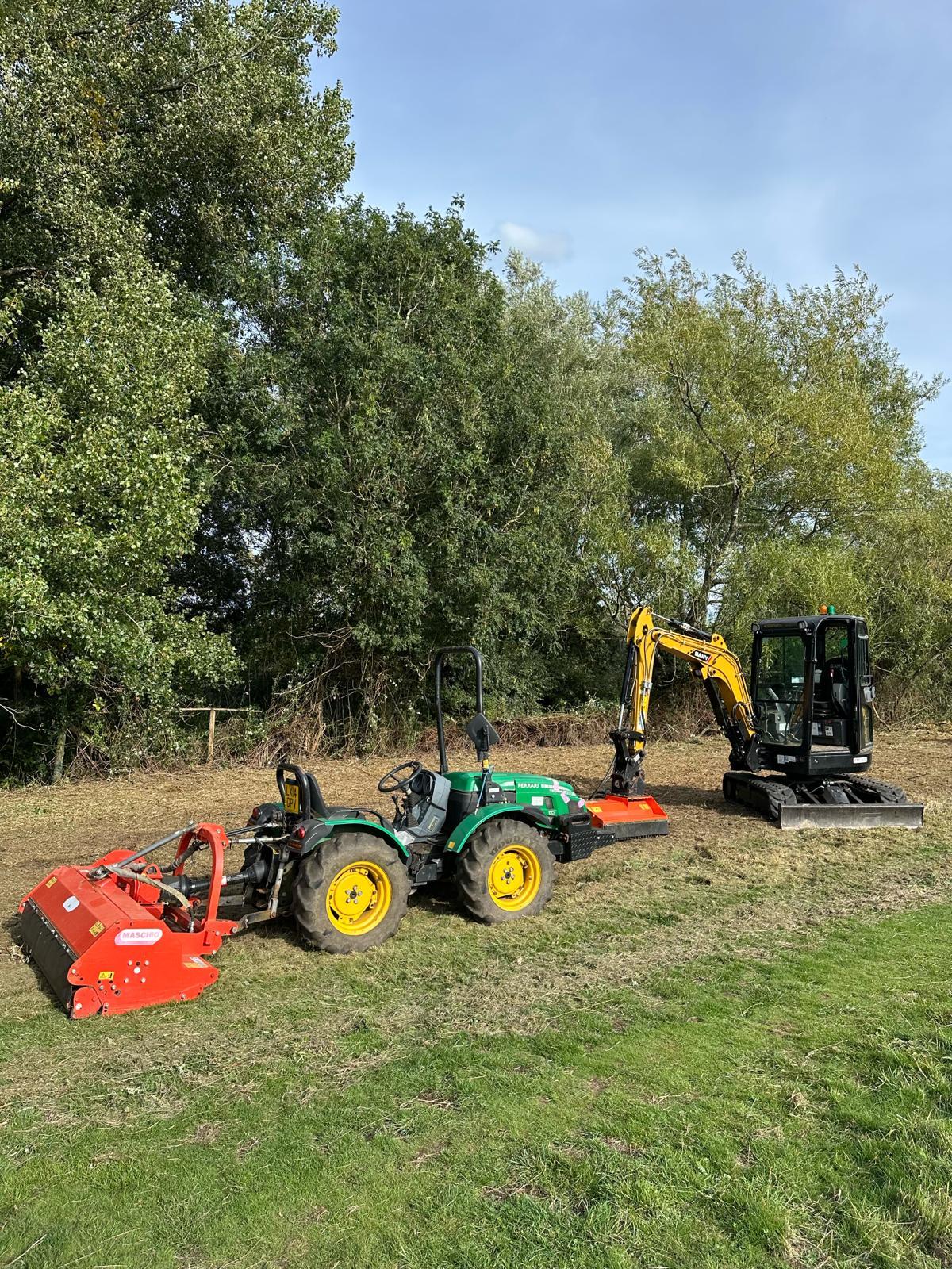 A compact tractor with a flail mower parked alongside a tracked excavator on a cleared site