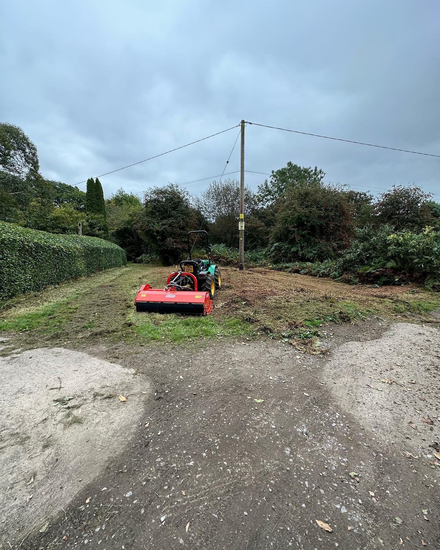 Flail mower clearing rough vegetation from a steep bank beside a track