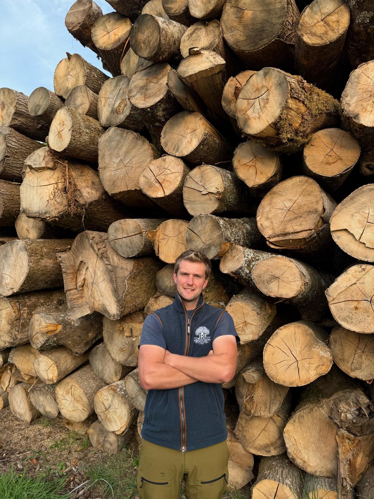 Joe Finnemore of JRF Contracting standing in front of a large stack of cut timber