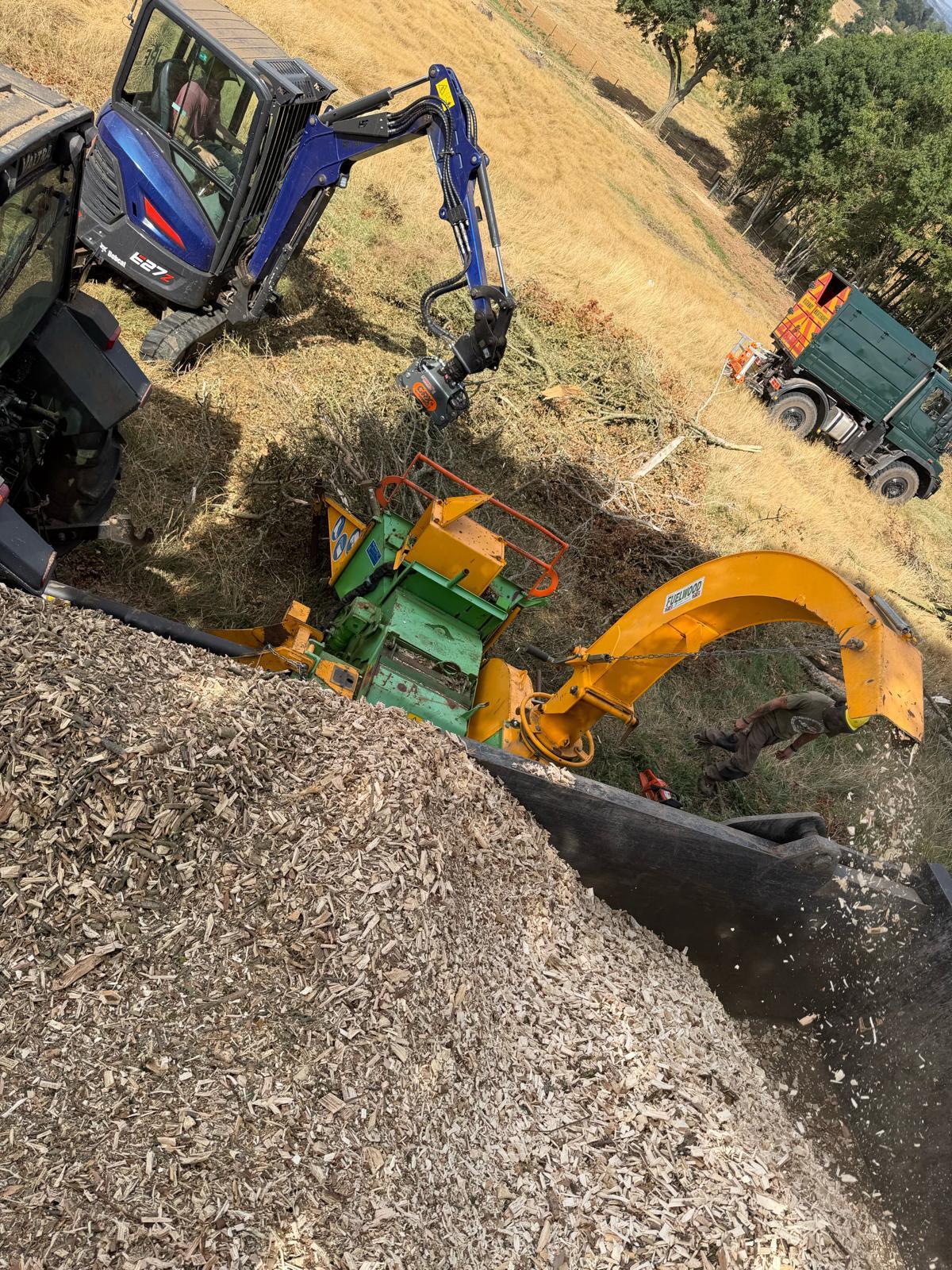A large heap of fresh wood chip beside the chipper and excavator that produced it